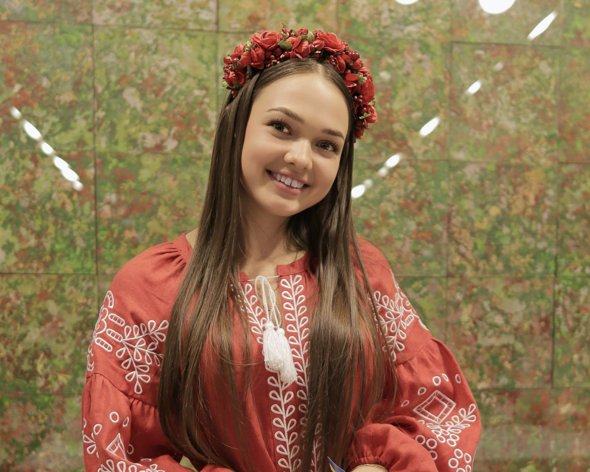 Woman in a red embroidered dress holding a cupcake in front of a decorative wall.